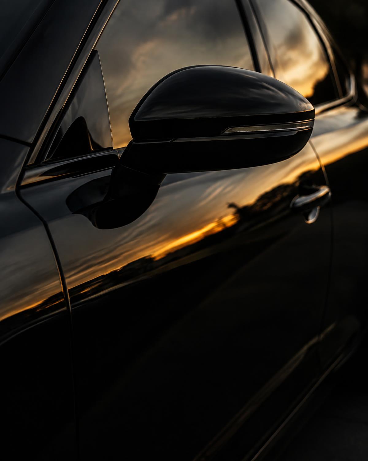 Detailer wiping down a gleaming dark car at golden hour in a driveway